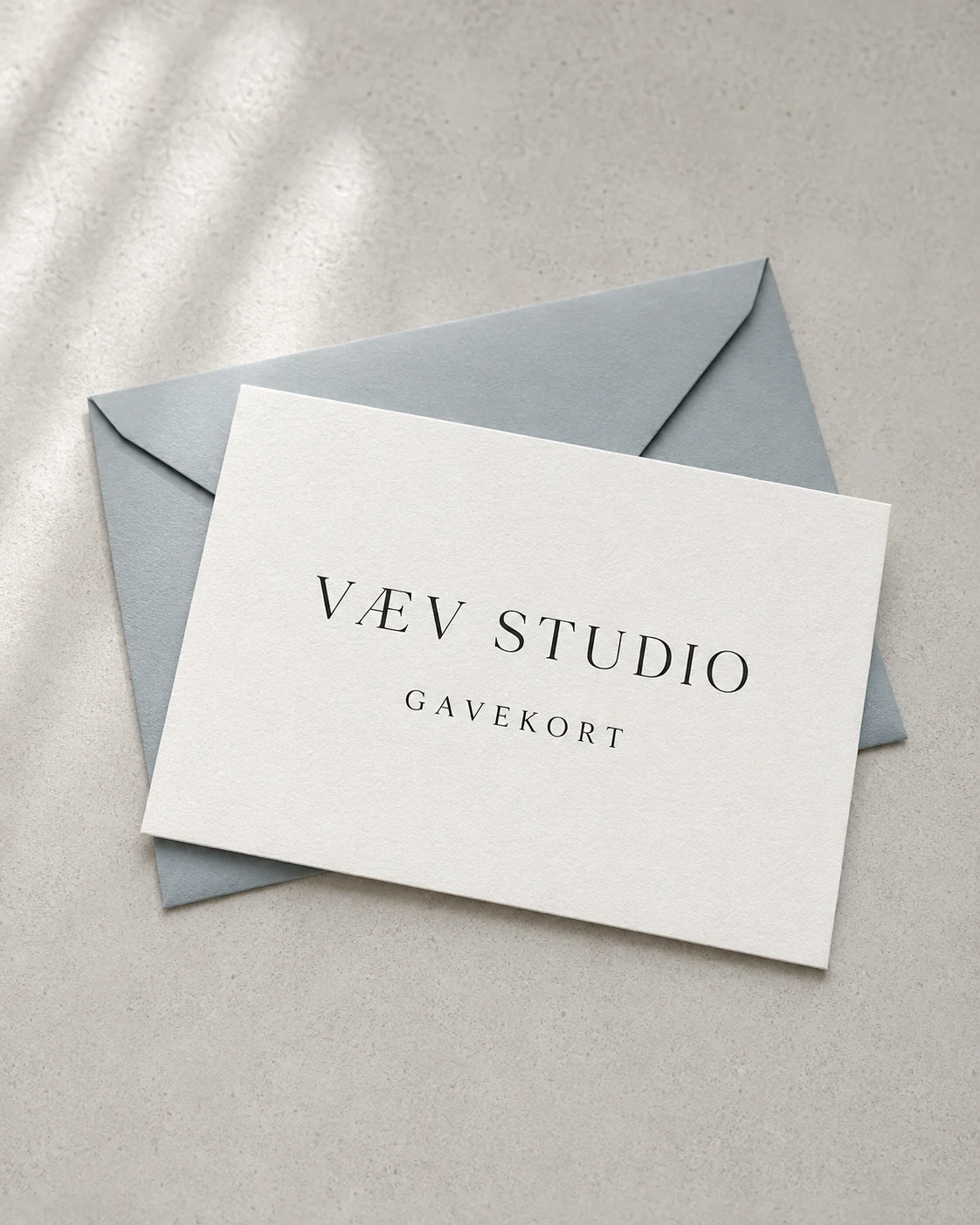 Porcelænshvidt VÆV STUDIO gavekort på en blågrå kuvert